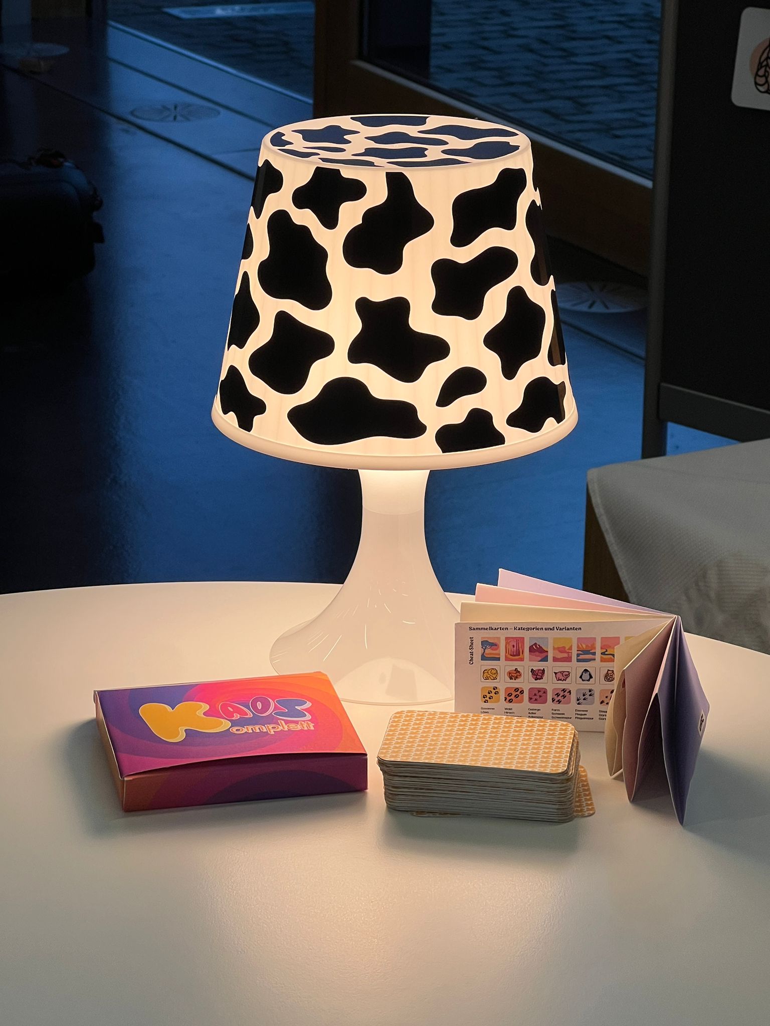 KaosKomplett card game prototype on a table with lamp